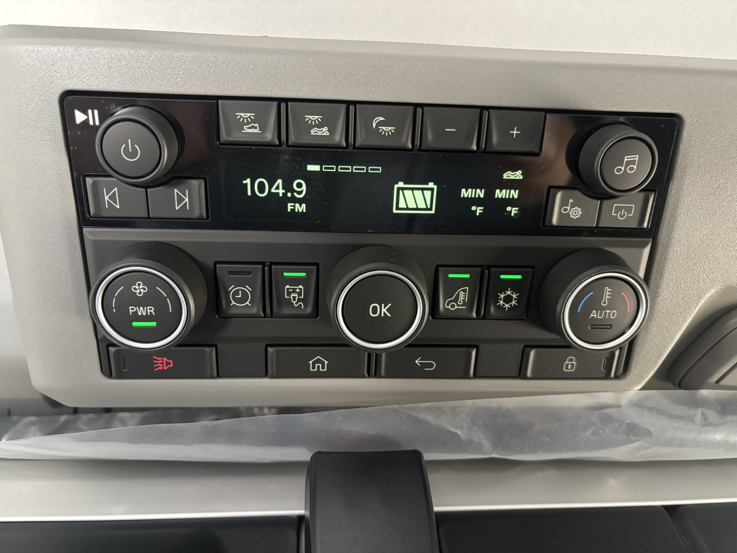 Truck cab dashboard showing radio controls at 104.9 FM, climate and media buttons, OK button in center, various knobs and icons.