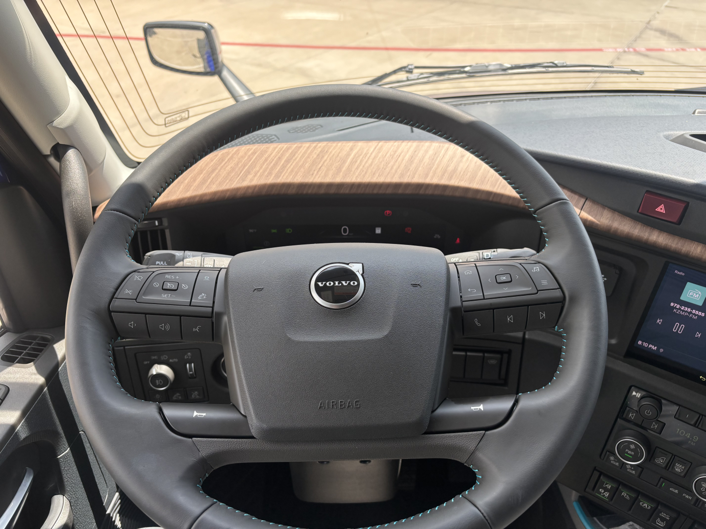 Volvo VNL steering wheel with Volvo emblem and control buttons in cabin, dashboard and infotainment visible.