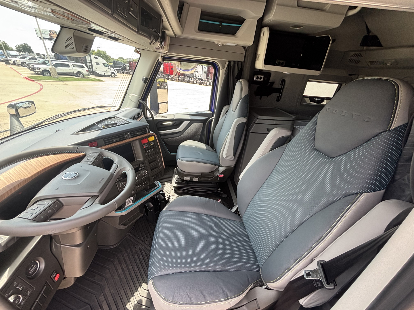 Cab interior of a Volvo VNL64T860 truck showing steering wheel, dashboard, and captain seats with blue fabric upholstery and overhead storage compartments.