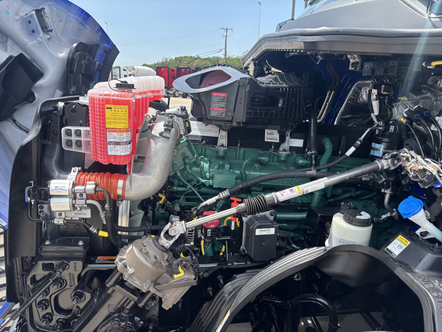 Volvo VNL64T860 engine bay showing diesel engine with green block, red coolant reservoir, white coolant reservoir, and various hoses and wiring.
