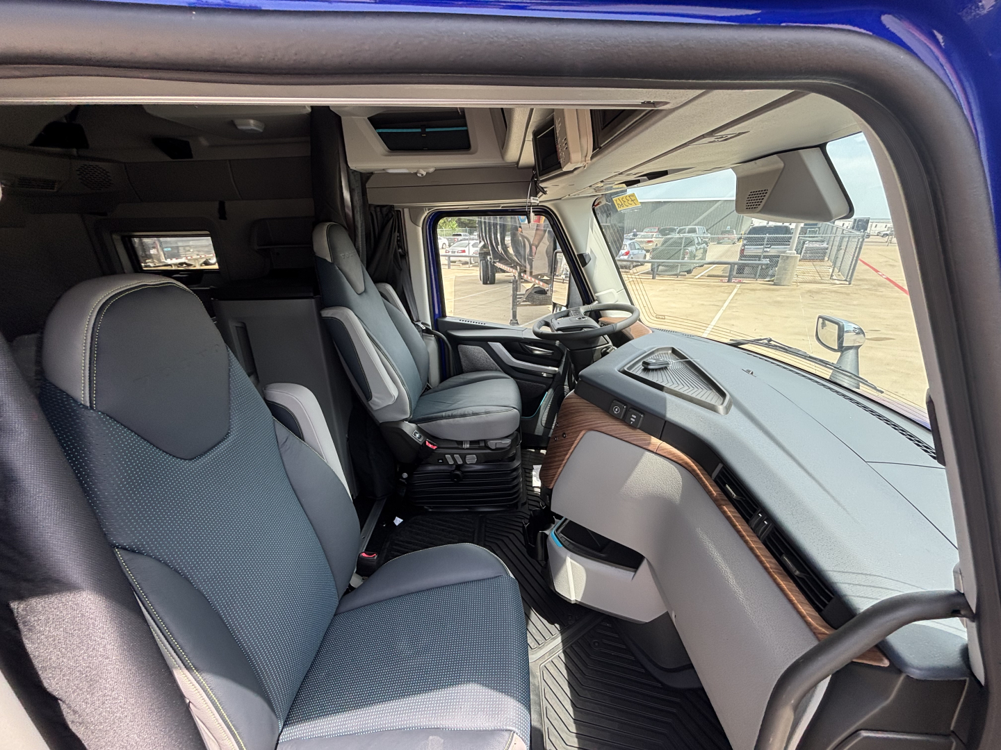 Volvo VNL interior showing driver's seat, passenger seat, dashboard, and center console with fabric seats and wood trim along the dash.