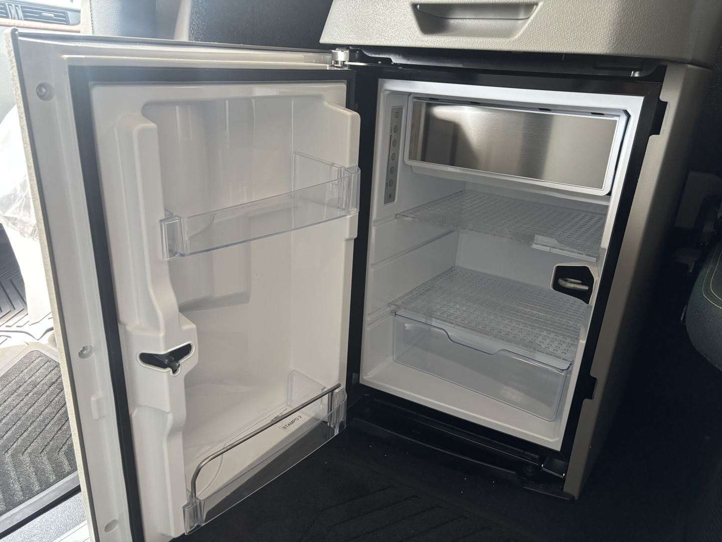 Volvo VNL64T860 truck interior showing compact refrigerator/freezer unit inside a galley with open door and empty shelves.