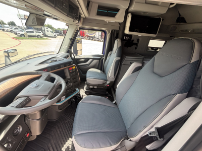 Cab interior of a Volvo VNL64T860 truck showing steering wheel, dashboard, and captain seats with blue fabric upholstery and overhead storage compartments.