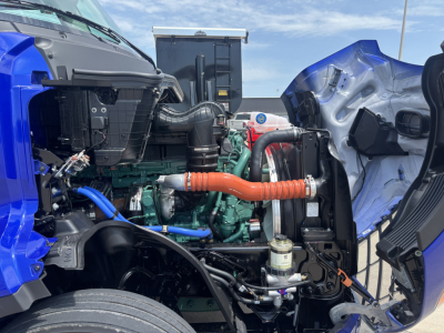 Volvo VNL64T860 engine bay view showing turbo hoses, coolant lines, and hydraulic components with blue cab exterior visible.