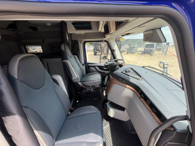 Volvo VNL interior showing driver's seat, passenger seat, dashboard, and center console with fabric seats and wood trim along the dash.