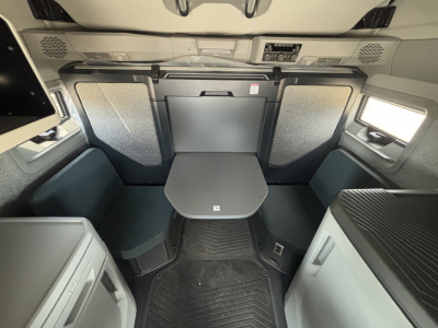 Interior cabin of a 2027 Volvo VNL64T860 sleeper showing front table/dinette area with fold-down seats and compact TV shelf; overhead dash cluster at front.