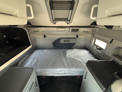 Truck interior sleeper cab with bed platform and overhead storage, Volvo branding not visible, window on right, center console and control panel above bed.