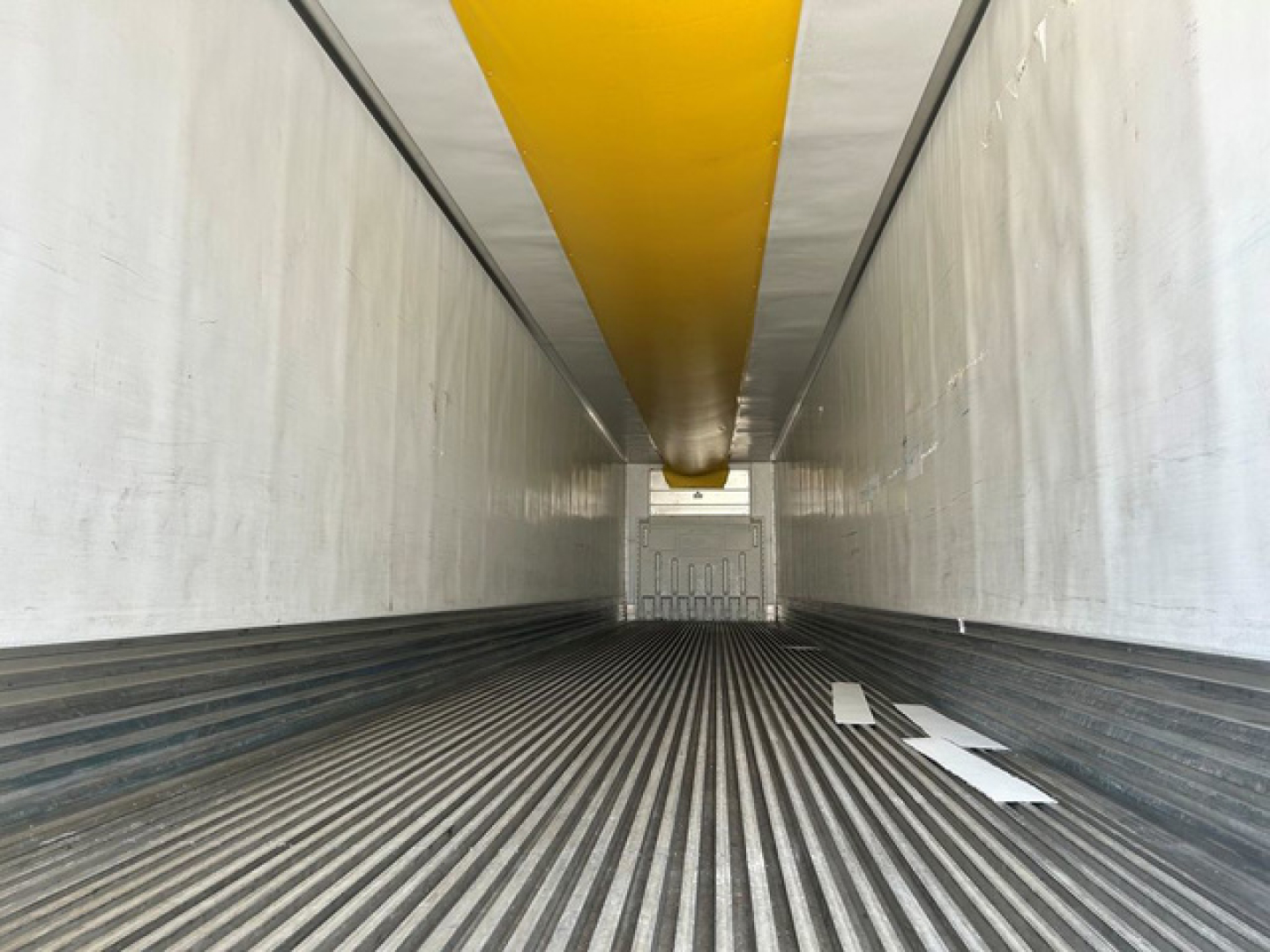 Interior of a refrigerated trailer with striped floor and yellow ceiling beam, empty cargo space.