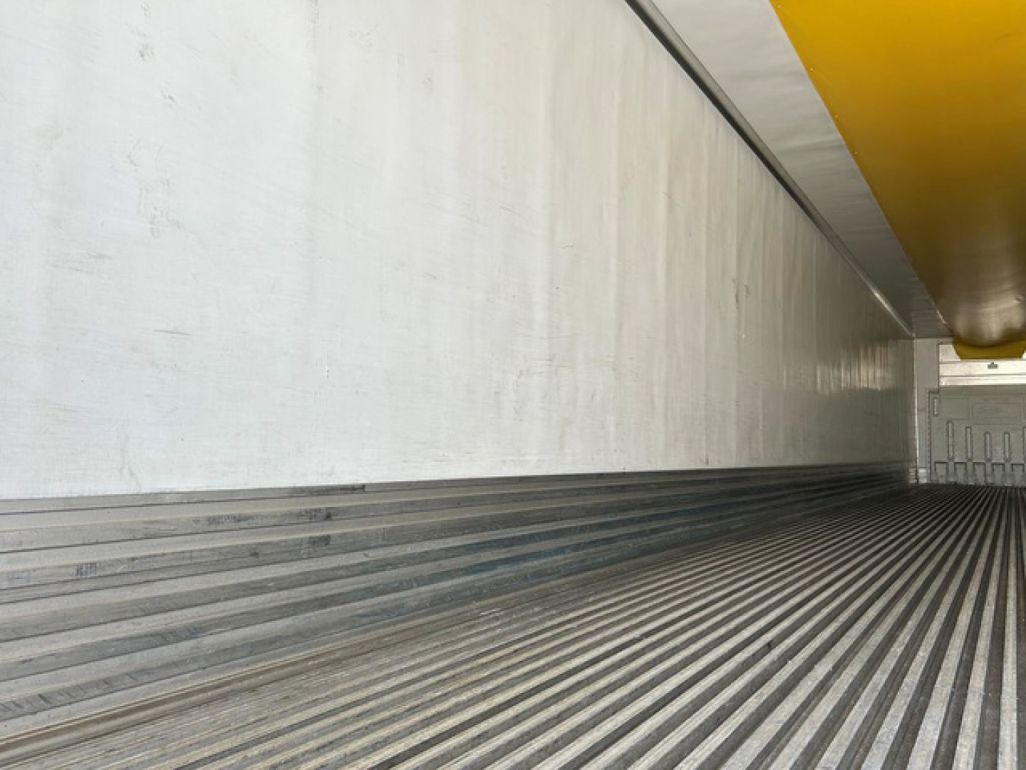 Trailer interior revealing corrugated floor and sidewall with yellow overhead cowling in a refrigerated trailer.
