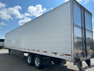 Utility reefer trailer side view showing aluminum walls, dual rear doors with diamond plate and hinges, dual rear axles, and reflective tape along lower edge.