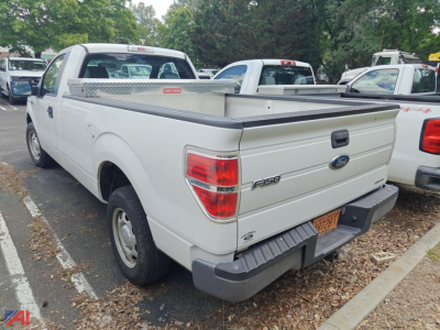 Ford F-150 pickup truck with a silver diamond plate utility bed in a used vehicle lot; rear view showing F-150 badge and taillights.