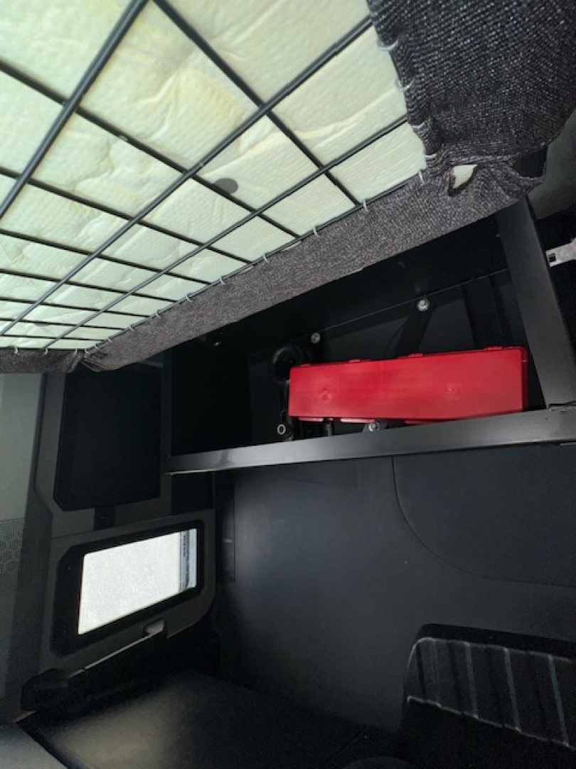 Trucks interior cargo area showing a red horizontal tool/seat component mounted under a grid-protected ceiling with insulation.