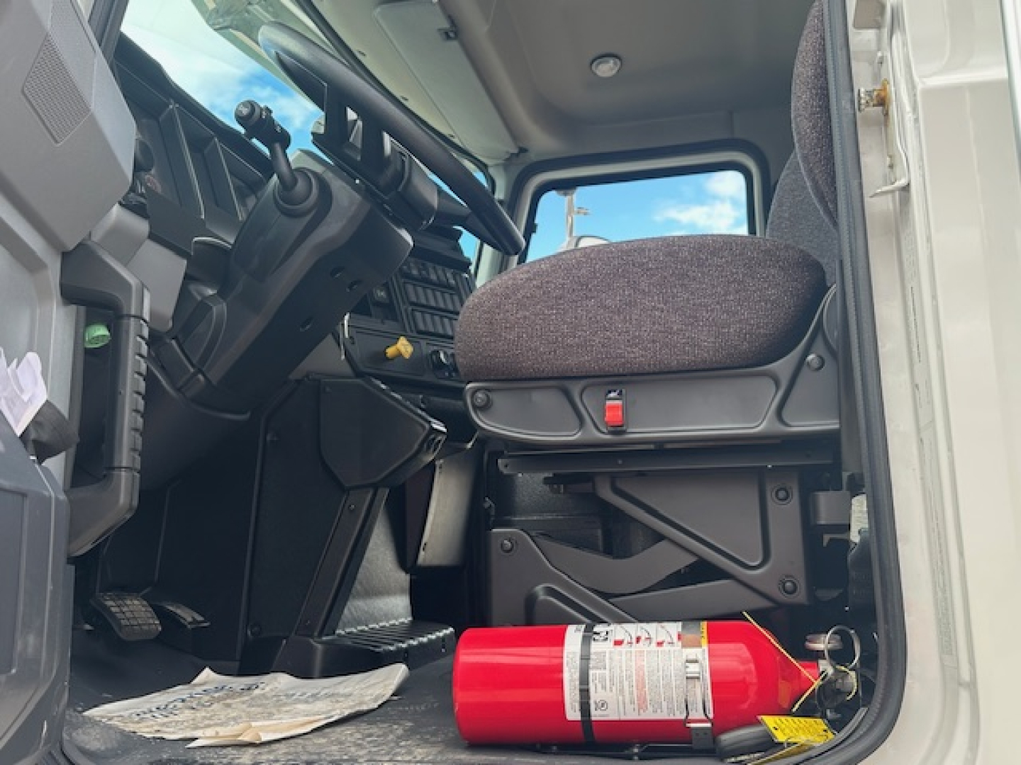 Truck cab interior showing driver seat and steering wheel of a Mack MD7 with a fire extinguisher on the floor.