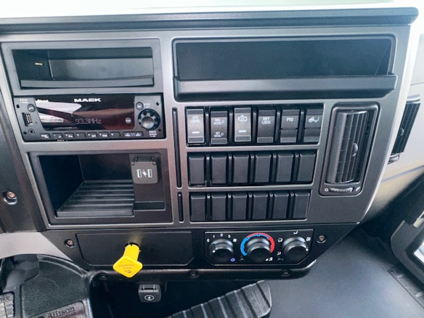 Dashboard of a Mack MD7 truck showing radio, switches, climate controls, and yellow dipstick handle visible in lower area.