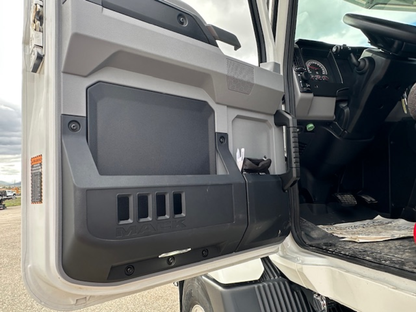 Truck cab interior door panel and open driver door showing dashboard and pedals in a 2025 Mack MD7.