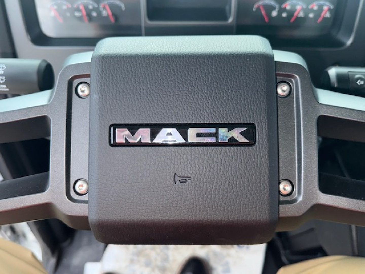 Mack MD7 steering wheel center with MAC K logo and dashboard gauges visible in background.