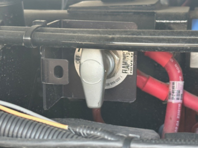 Trucks bay showing battery disconnect switch with label, red battery cables, and wiring harness in a Mack MD7 engine area.