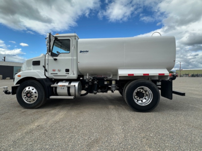 Mack MD7 tanker truck in side view showing stainless fuel tank and cylindrical aluminum tank body with signage
