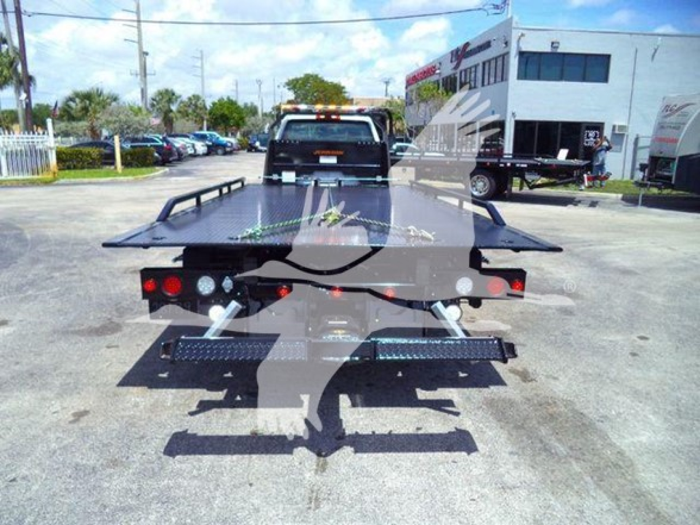 Flatbed rollback tow truck rear view with loading platform and rear lights visible.
