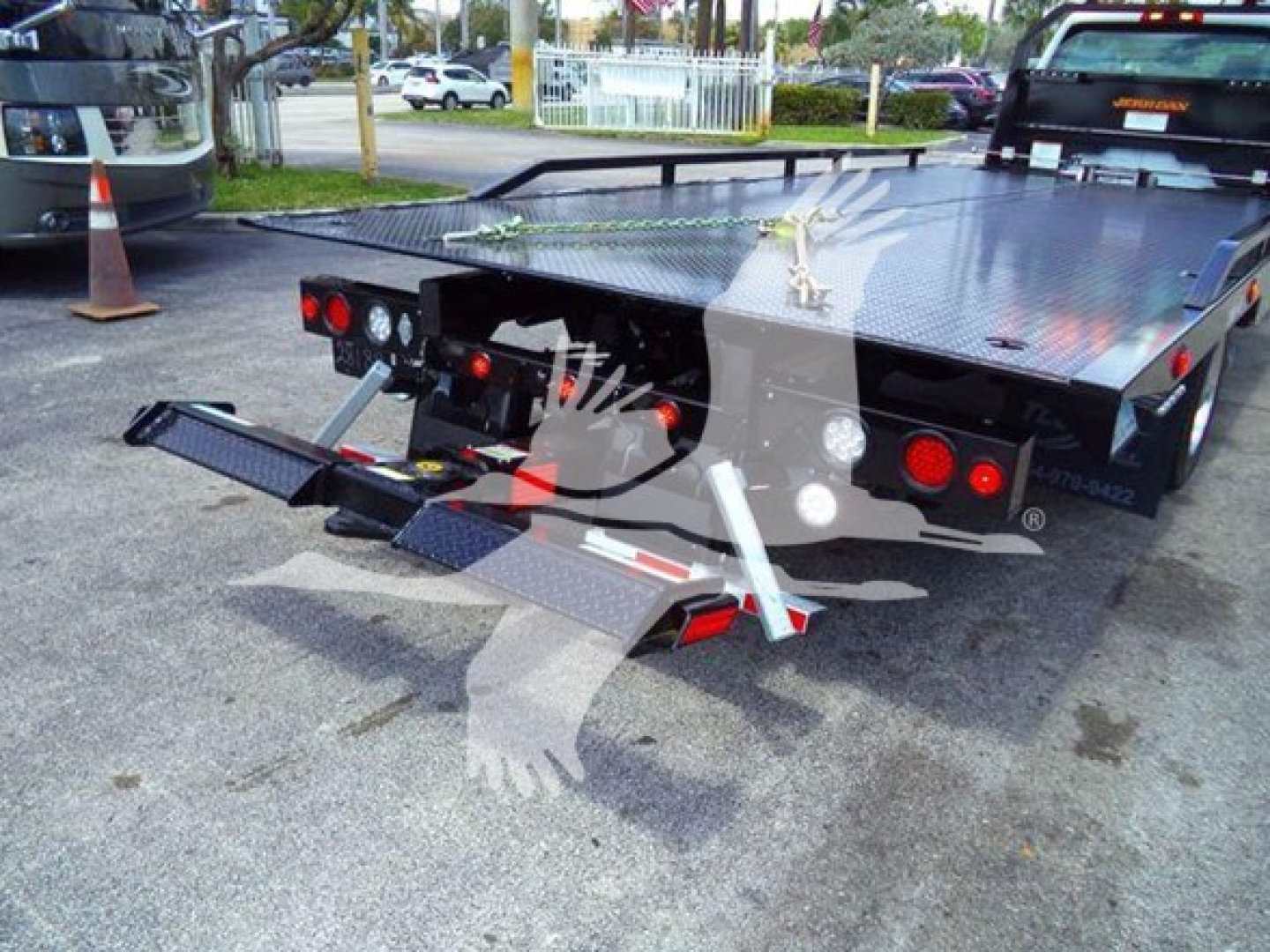 Back view of a flatbed tow truck with a hydraulic lift at the rear, diamond plate steel bed, and taillights visible.