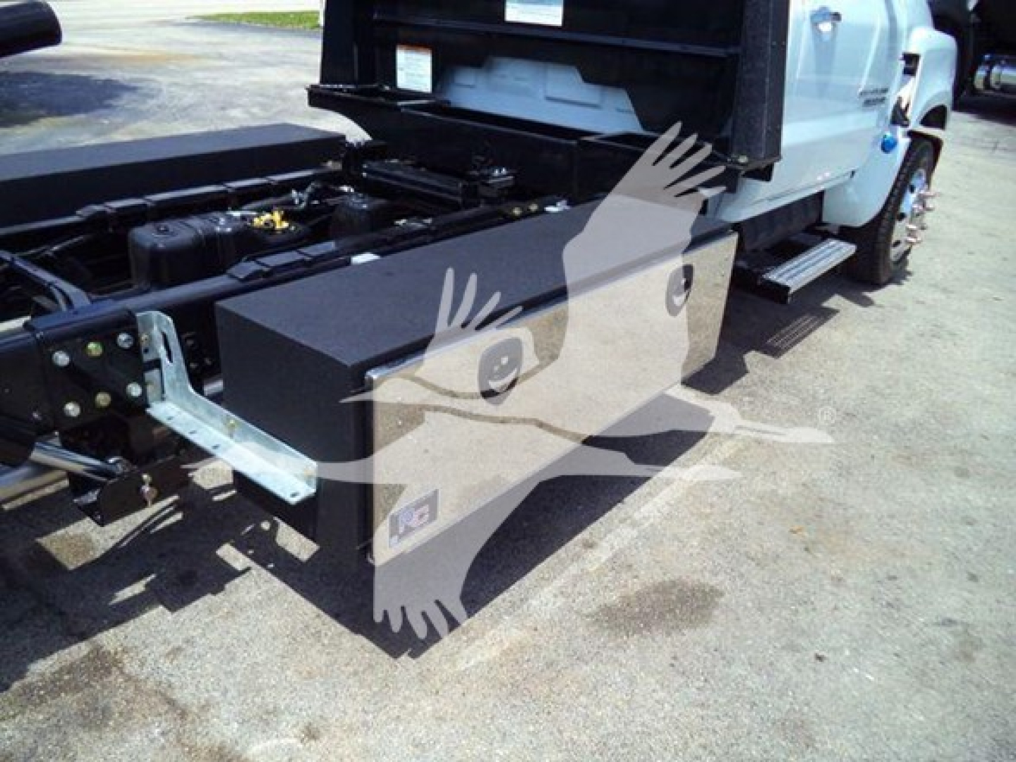 Truck bed area of a 2023 Chevrolet Silverado 6500HD rollback chassis showing a large rectangular toolbox mounted near the cab and side steps visible.