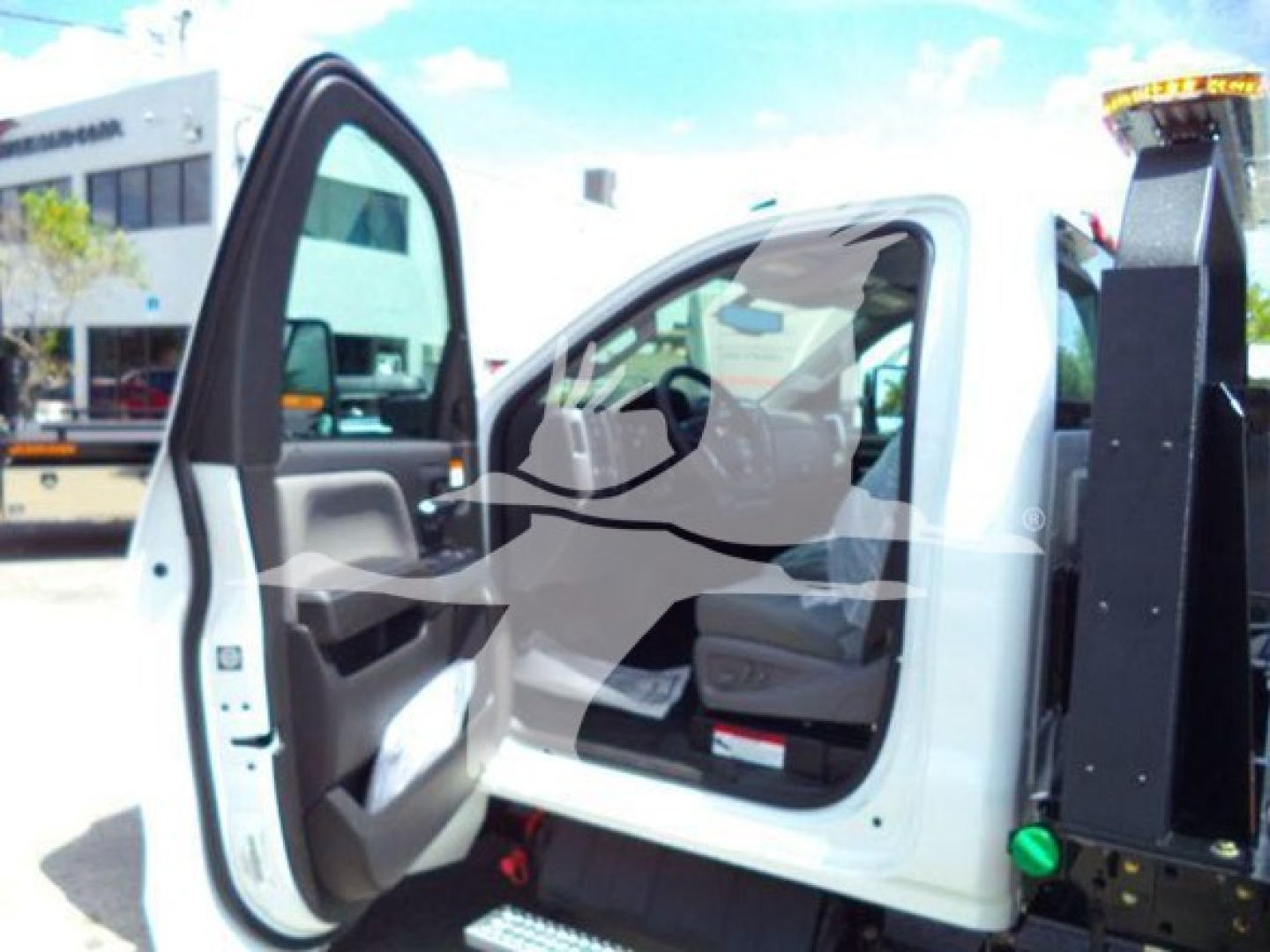 Trucks cab interior with open driver door; Silverado 6500HD rollback tow truck. Visible text: none legible inside cabin; exterior shows partial dealership lot.