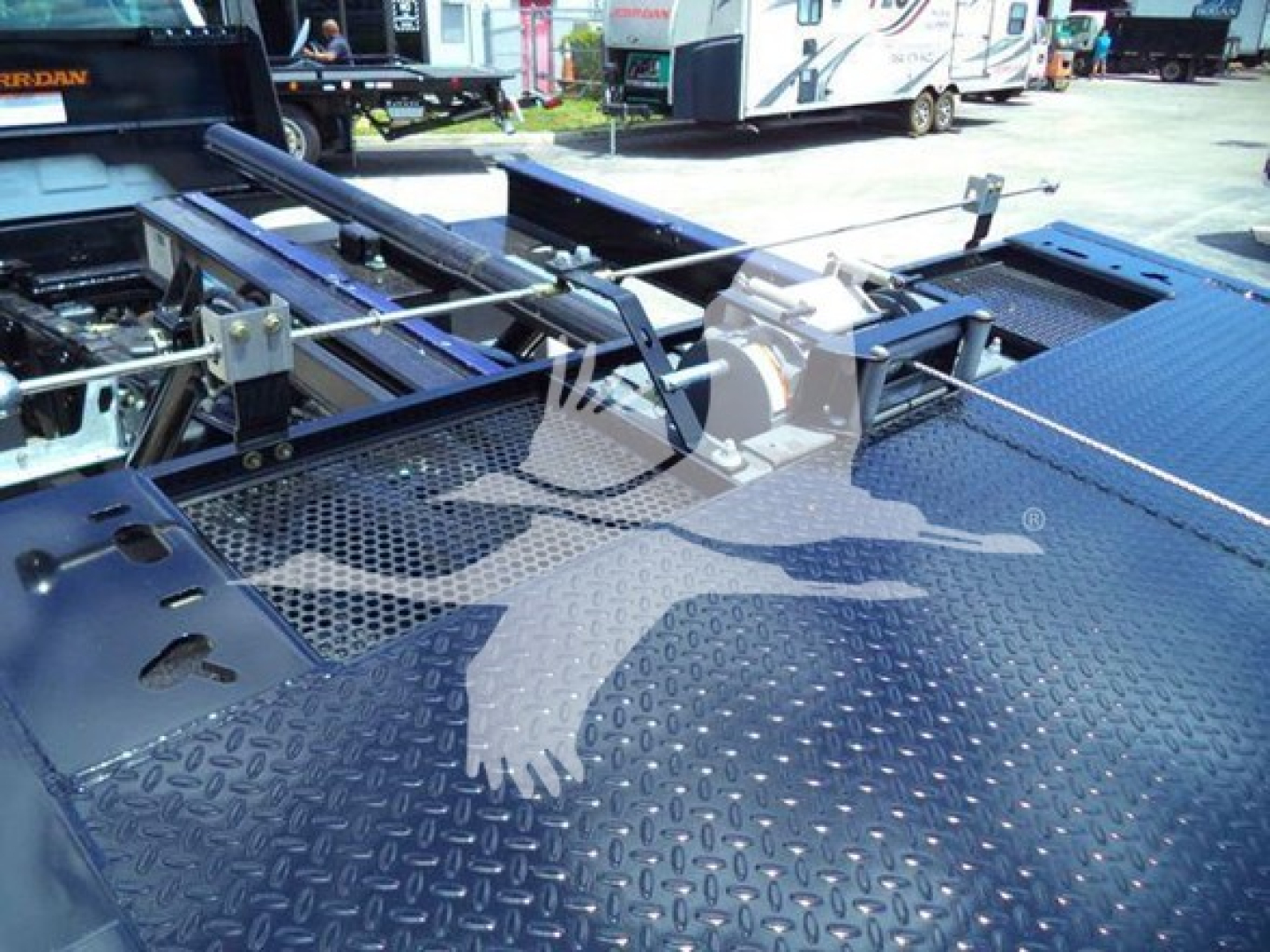Truck bed with hydraulic hardware and grab hooks; diamond plate surface; faint watermark logo overlapping.