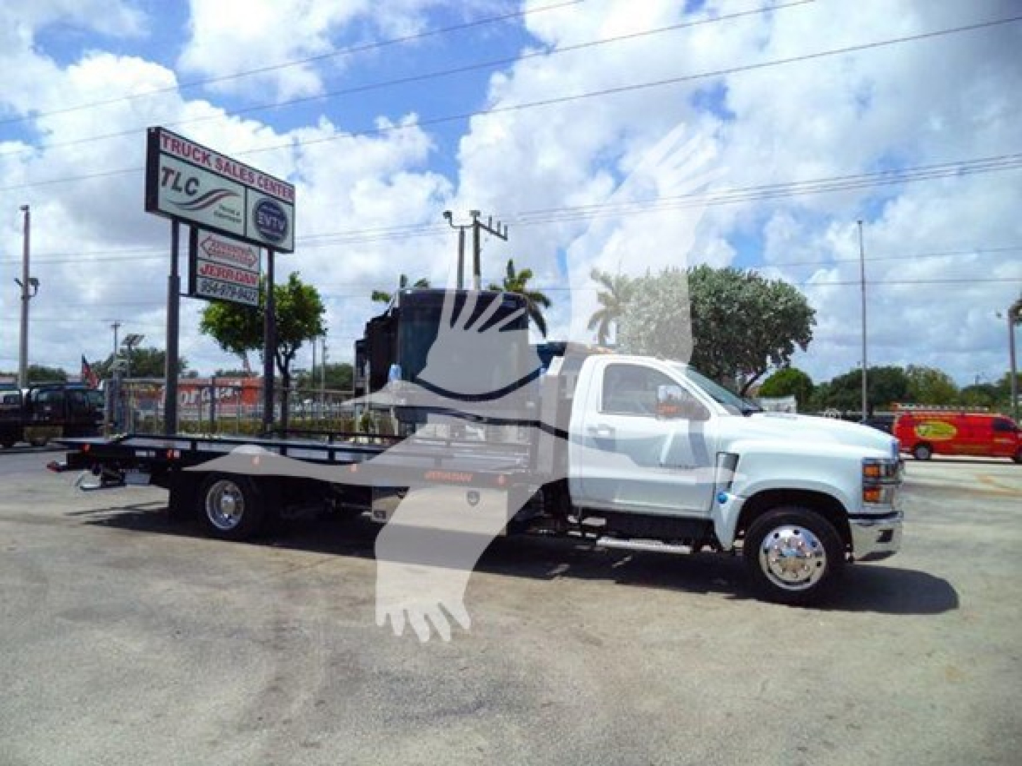 Truck used for rollback with flatbed attached, white Chevrolet Silverado 6500HD in a dealership lot, stock sign in background, blue sky