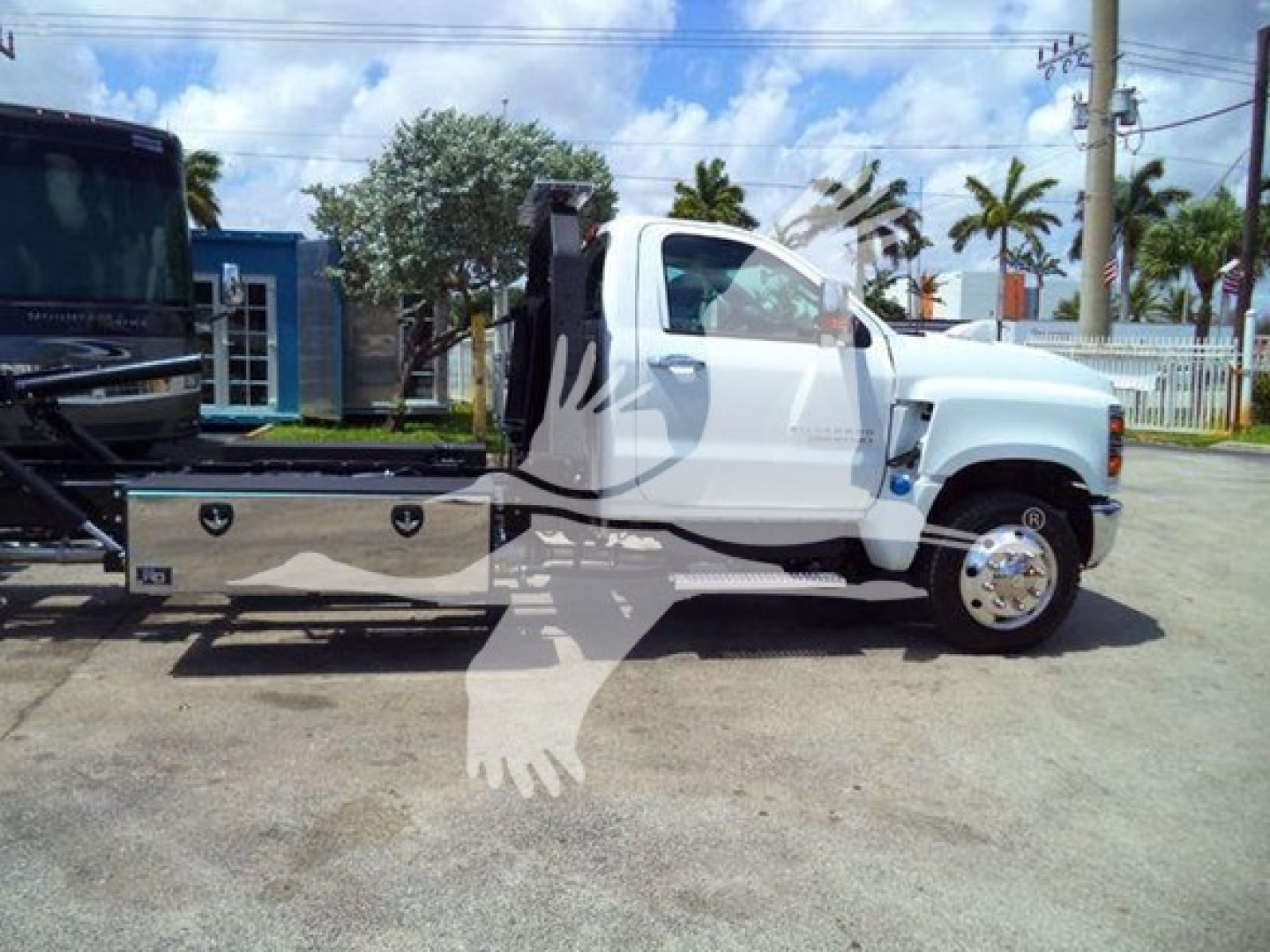 Flatbed rollback tow truck with white cab and aluminum toolboxes on the side, chevrolet-like hood; image shows the vehicle in a lot.