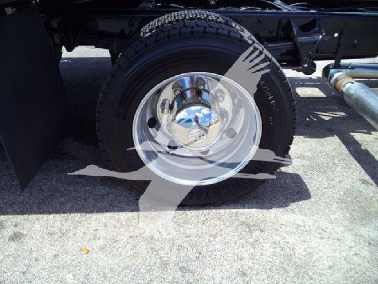 Wheel and tire on a Chevrolet Silverado rollback chassis showing chrome hubcap and steel drum, with undercarriage components visible.