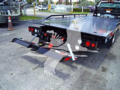 Back view of a flatbed tow truck with a hydraulic lift at the rear, diamond plate steel bed, and taillights visible.