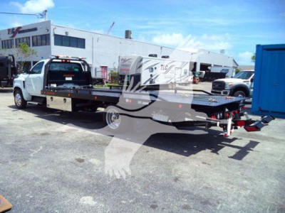Truck bed tow truck setup in a parking lot showing a rollback bed with crane, Silverado 6500HD label obscured by watermark through the image