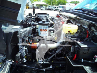 Truck engine bay showing radiator, hoses, and various fluid reservoirs.