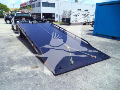 Flatbed tow truck trailer with a long blue metal deck and a gooseneck-style front, viewed from a slight angle in a dealership lot.