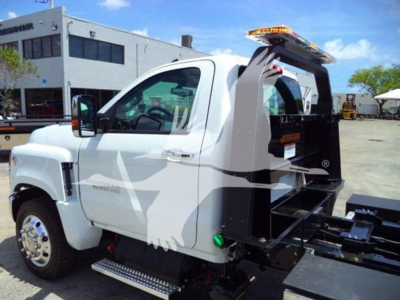 Truck side view showing a white 2023 Chevrolet Silverado 6500HD rollback with hydraulic bed and chrome wheels.
