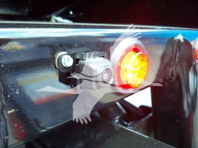 Vehicle tail light and hitch area with a circular red reflector and a black bracket; small silver sensor/connector visible.