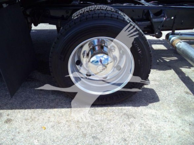 Wheel and tire on a Chevrolet Silverado rollback chassis showing chrome hubcap and steel drum, with undercarriage components visible.