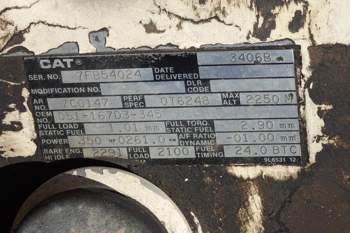 Cat engine block data plate showing serial number 7FB54024, date delivered, engine specifications, fuel and torque values, and various codes on a weathered metal plate.