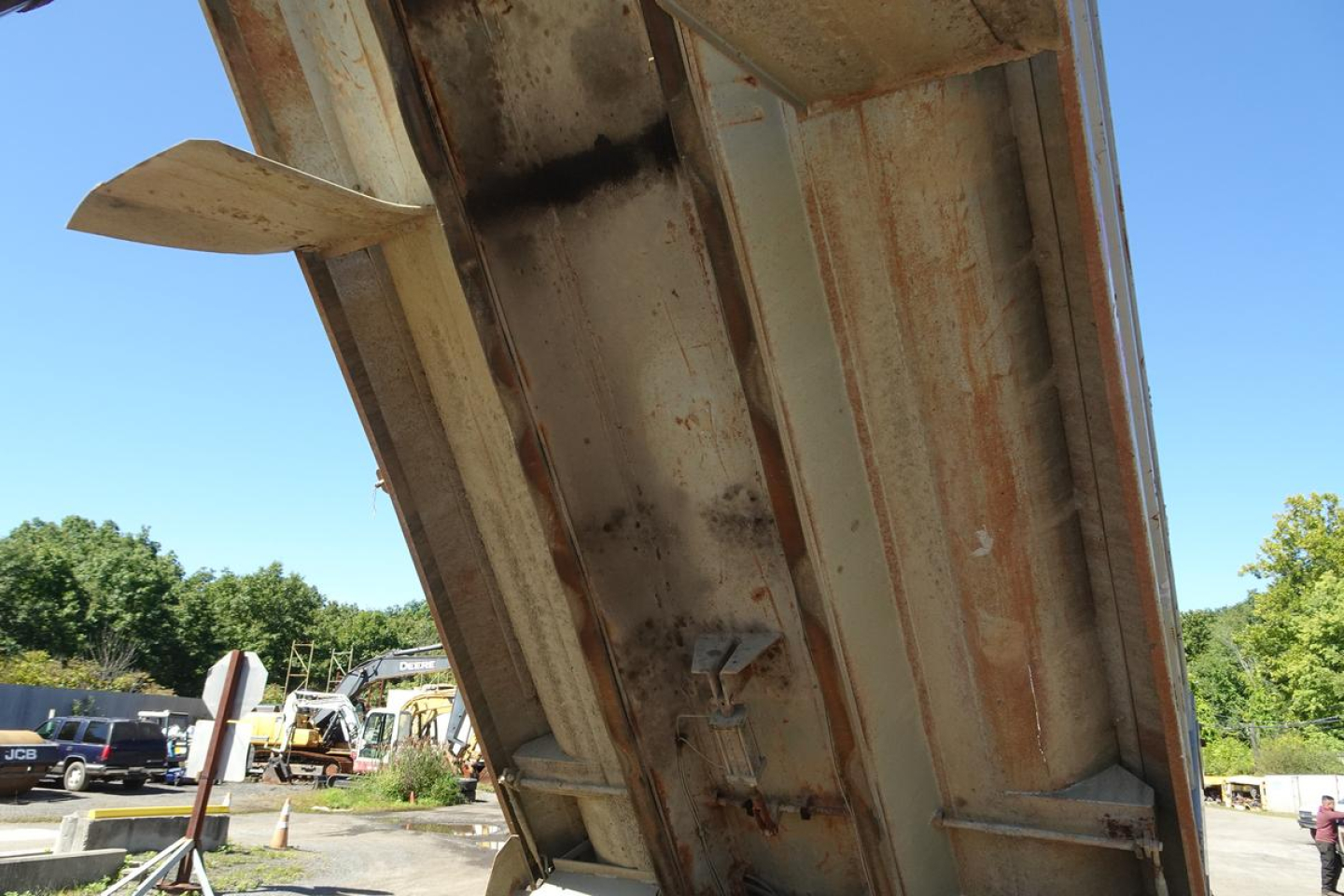 Dump truck bed underside showing steel frame with rust and dirt, side view of dump body in raised position