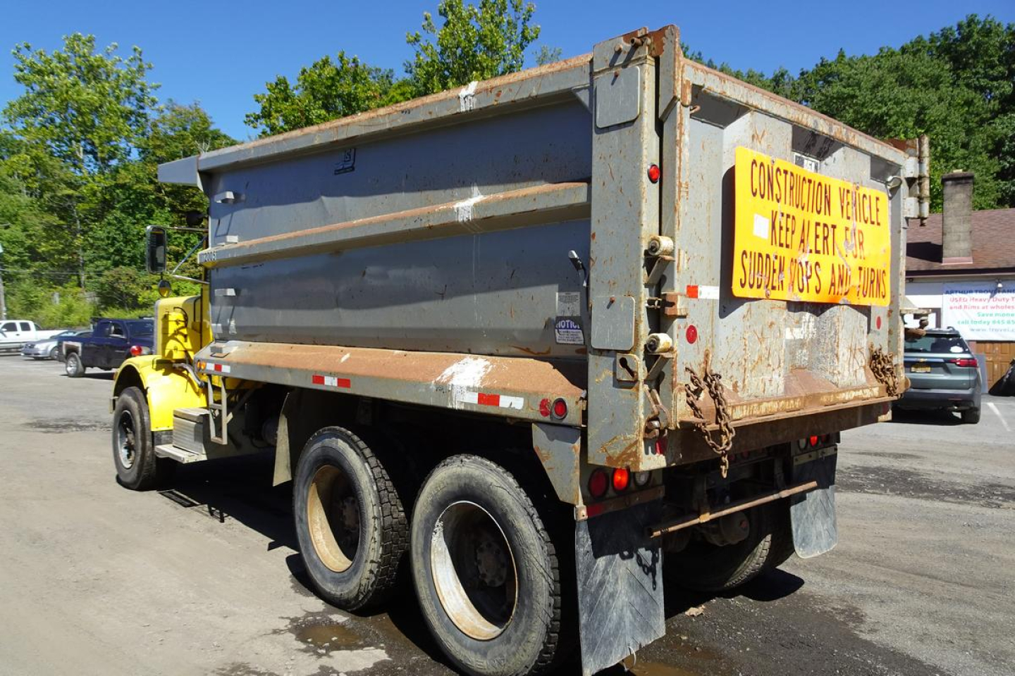 Peterbilt 359 dump truck in-service showing dual rear axles and a metal dump bed with a caution sign on the tailgate.