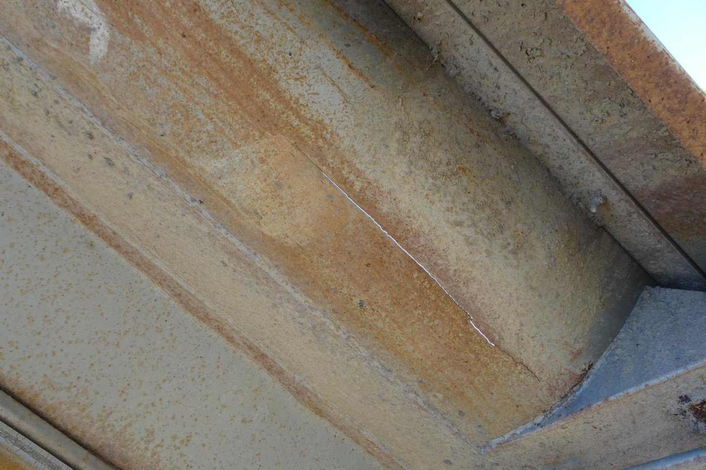 Dump truck bed interior seen with rusty corrugated metal surface and weld seam.