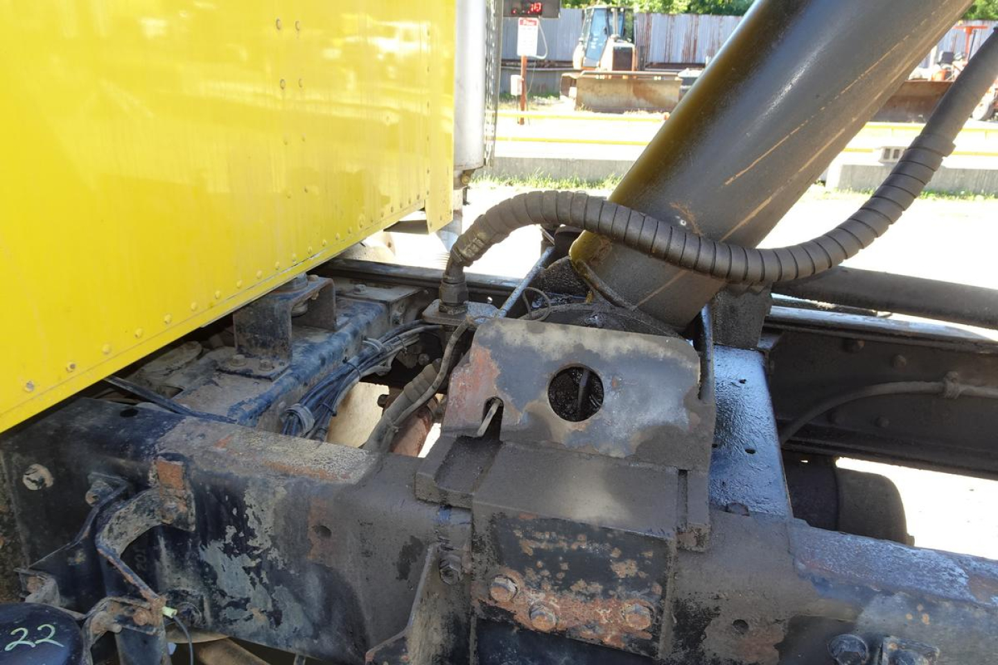 Peterbilt 359 dump truck chassis with hydraulic hoses and frame components visible under yellow cab, showing wear and dirt.
