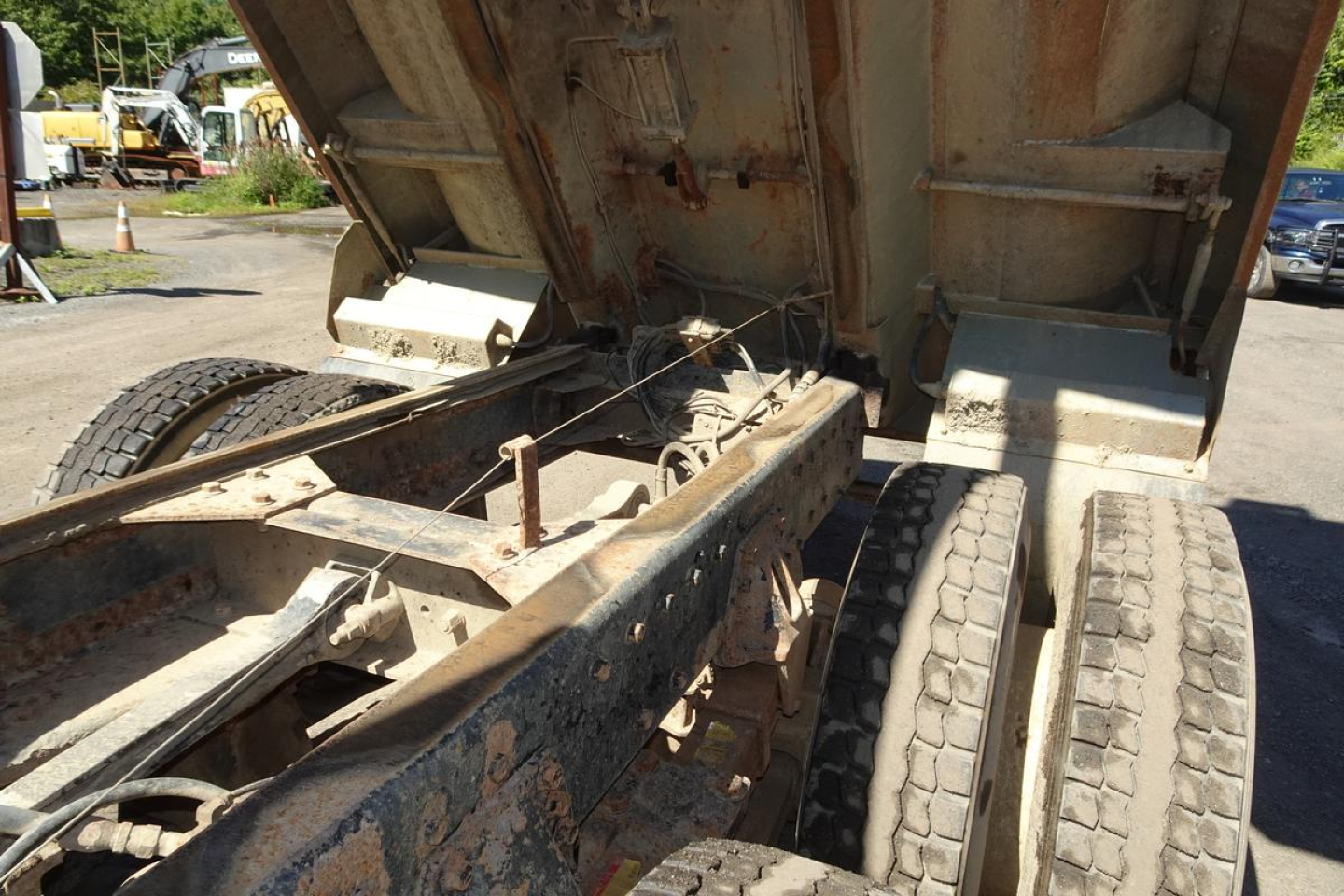 Peterbilt 359 dump truck frame and rear undercarriage with bed raised, showing dual rear wheels and rusted chassis components.