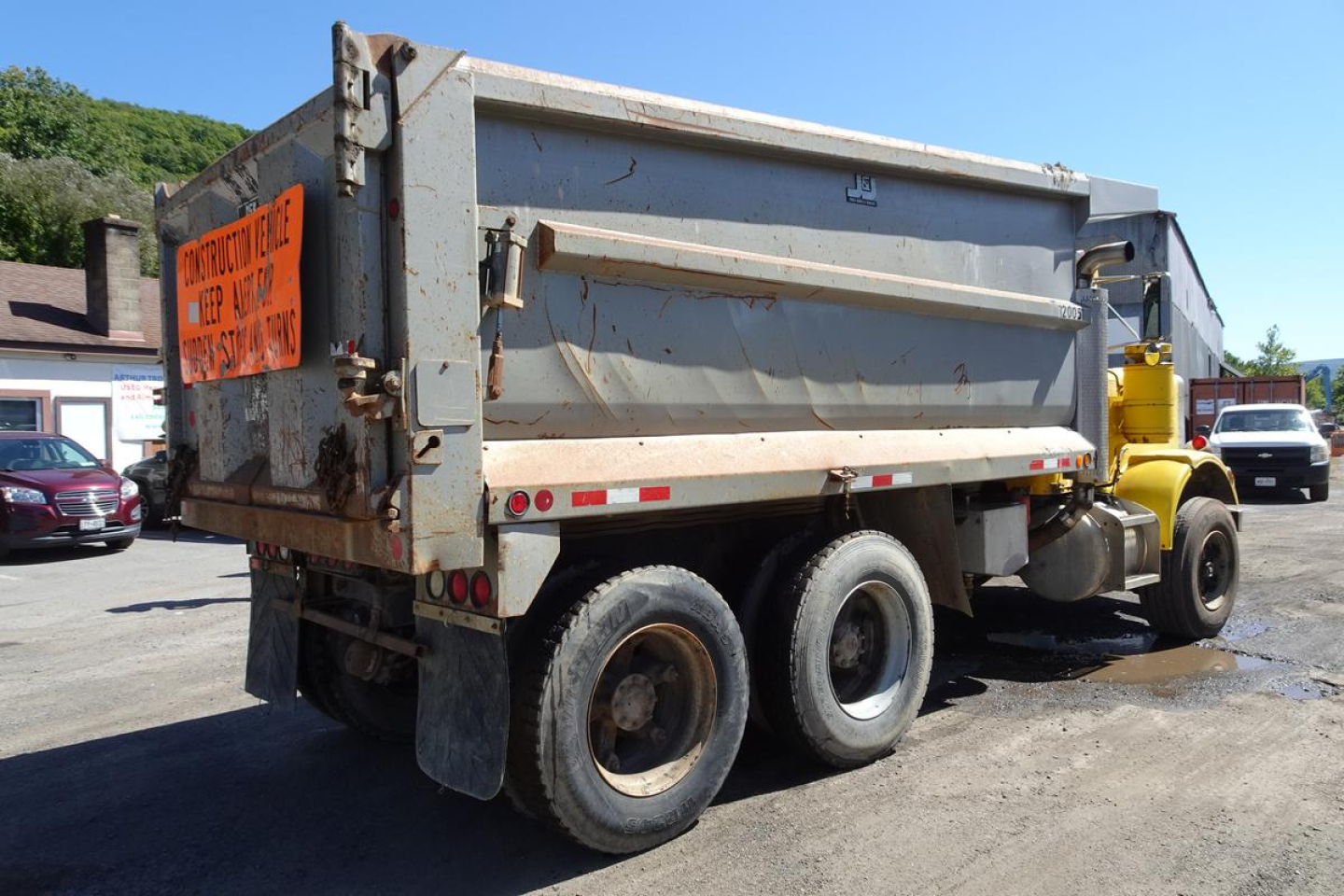 Peterbilt 359 dump truck in-service rear angle showing dump bed and rear wheels, with orange sign on tailgate.