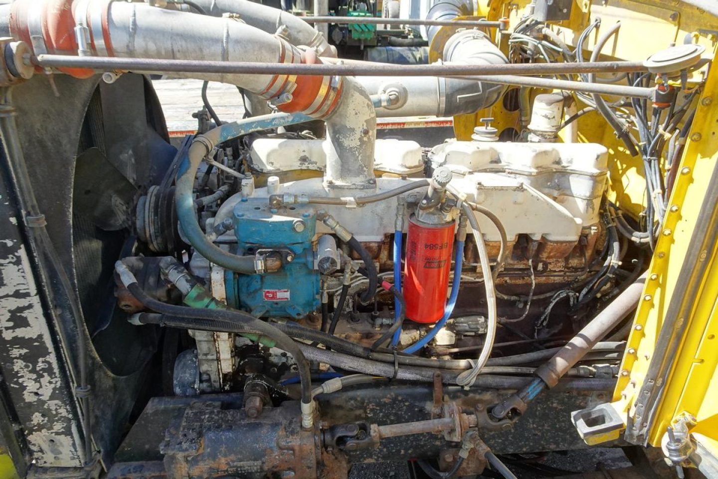 Peterbilt 359 engine bay showing diesel engine with air filter and hoses in-service; visible components include blue alternator, red oil filter, white air intake, and various metal pipes.