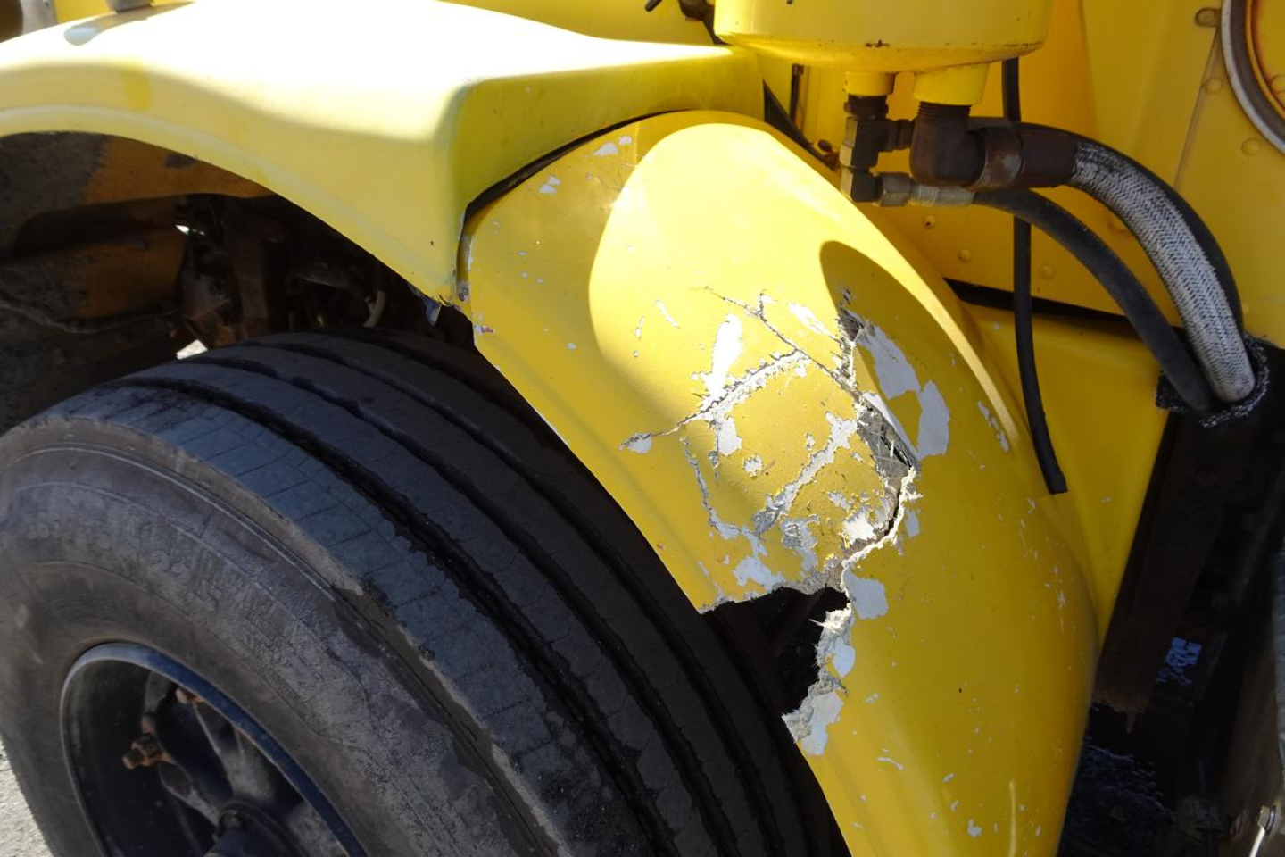 Peterbilt truck front fender with yellow paint and damaged paint around wheel well, heavy-duty tire visible.