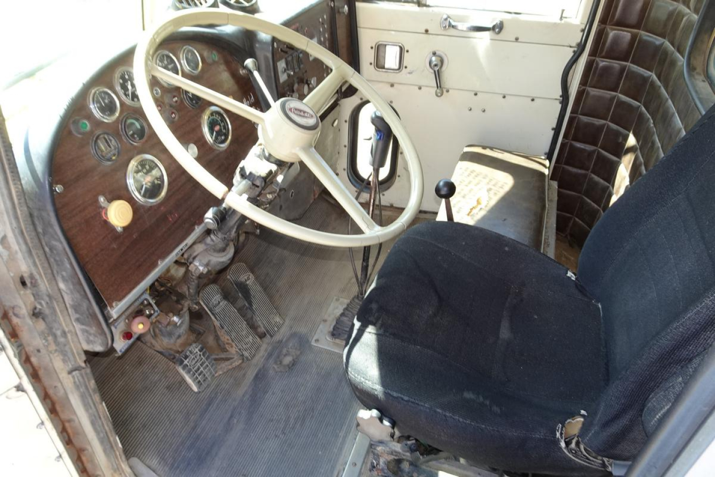 Peterbilt 359 truck interior showing wooden dashboard, round gauges, cream steering wheel, manual gear shifter, and worn black driver's seat.
