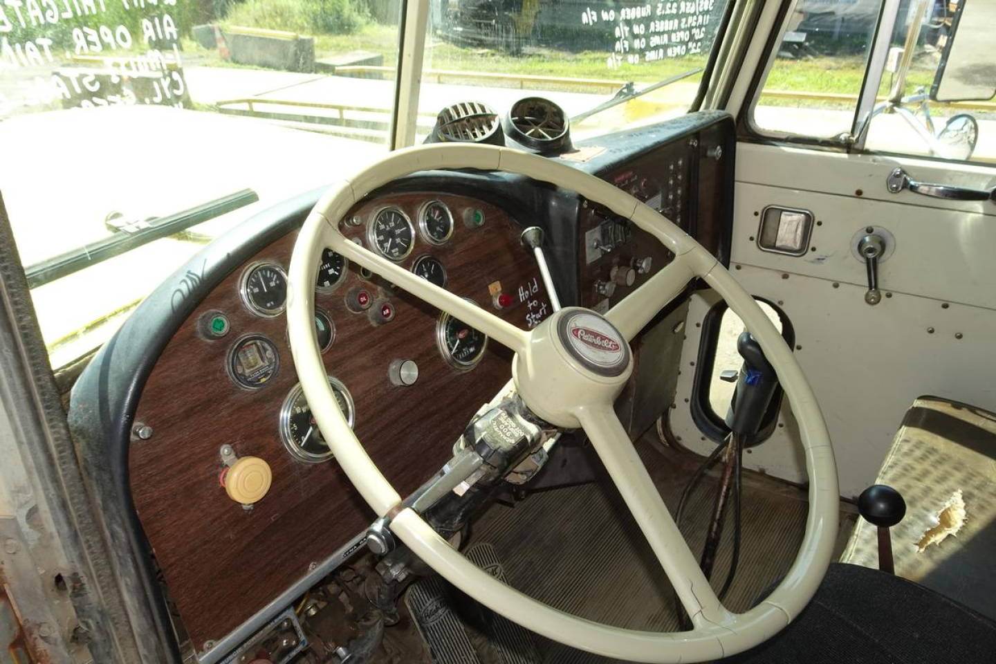 Peterbilt truck cab interior showing steering wheel, dashboard gauges, and worn door panel.