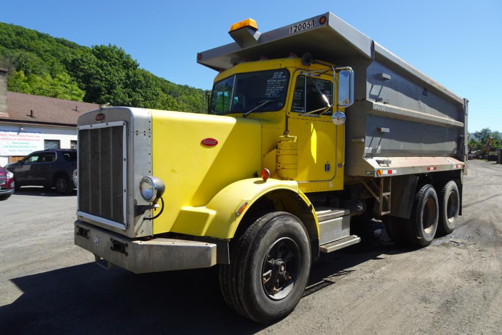 Peterbilt dump truck in yellow with grey dump body, front grille, and dual rear axles; side view shows HINO? branding on cab? No; image shows yellow Peterbilt 359 dump truck in a yard.