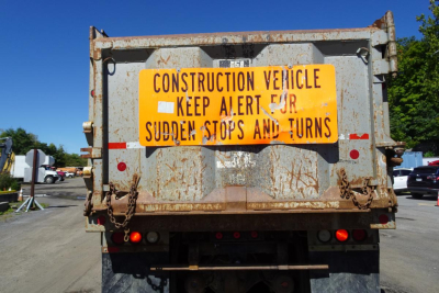 Rear view of a used 1986 Peterbilt 359 dump truck with a bright orange construction warning sign on the tailgate.